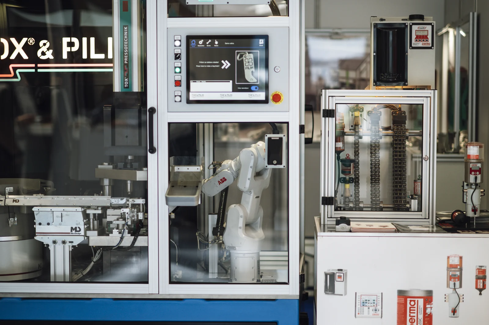 An industrial robot arm working inside an enclosed automated manufacturing cell with controls, tooling and conveyors visible.